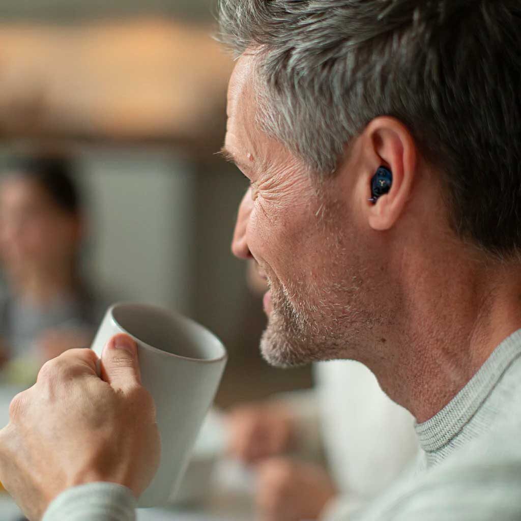 Man in a coffee shop using Soundgear bluetooth hearing protection.